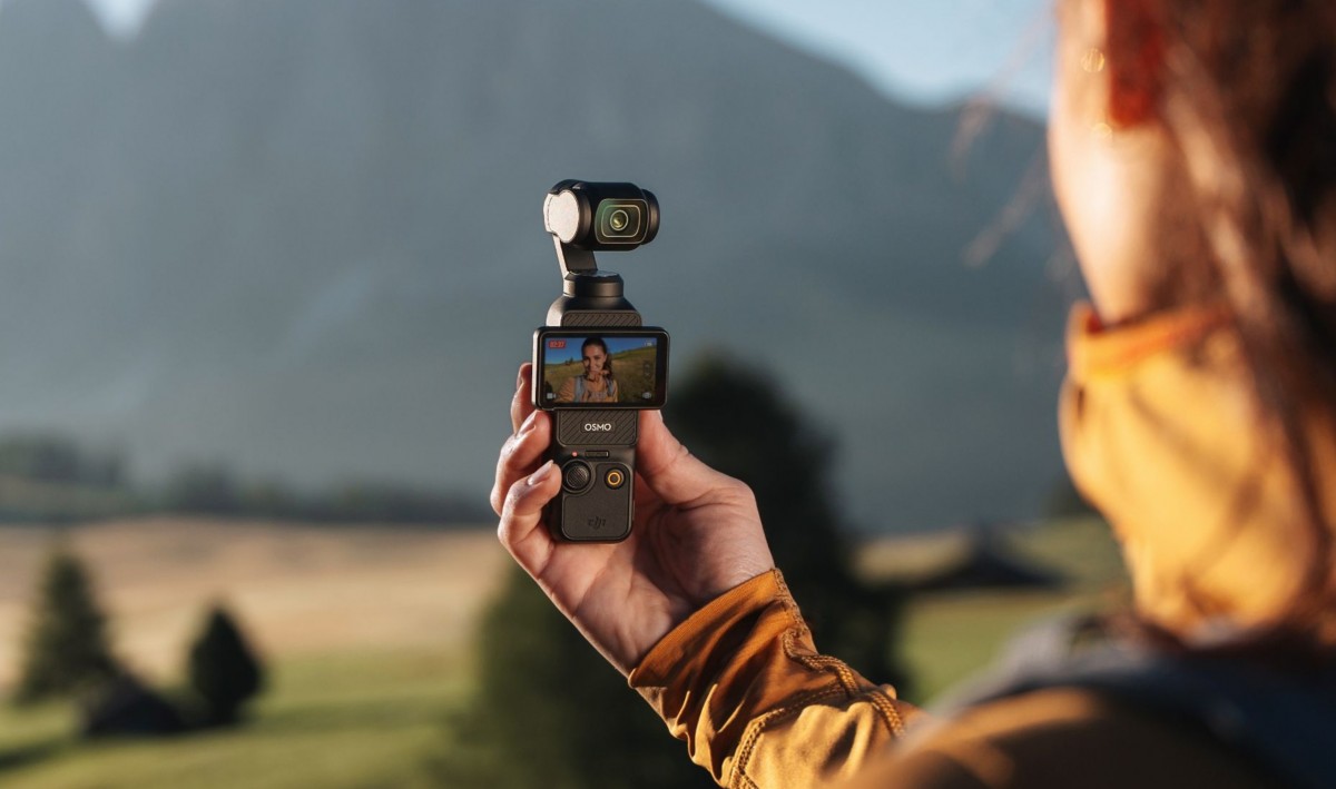 فردی که دوربین DJI Osmo Pocket 3 را در دست گرفته و در حال فیلمبرداری از یک منظره کوهستانی است.