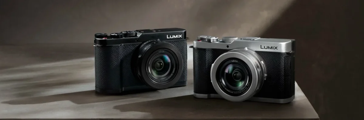 دو دوربین Lumix با بدنه نقرهای و مشکی کنار هم روی سطح روشن در نور استودیویی.